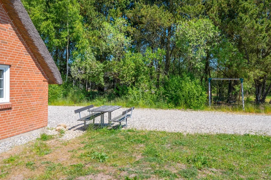 Una mesa de picnic está junto a un edificio de ladrillo, con árboles al borde del área de grava.