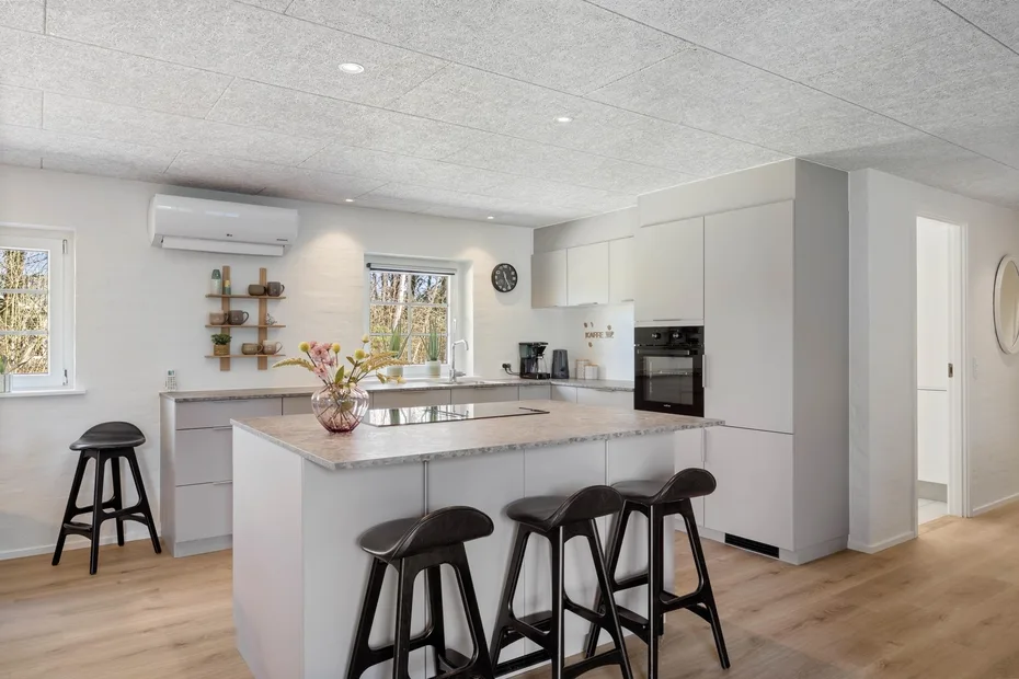 Una cocina luminosa con una isla central, asientos oscuros y armarios blancos.