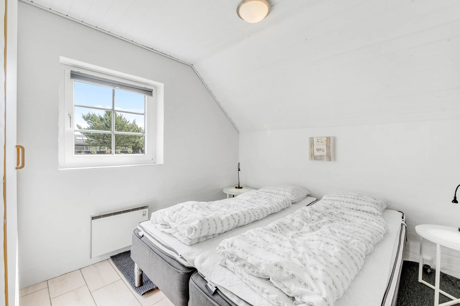 Un dormitorio luminoso con dos camas bajo un techo inclinado y una ventana.