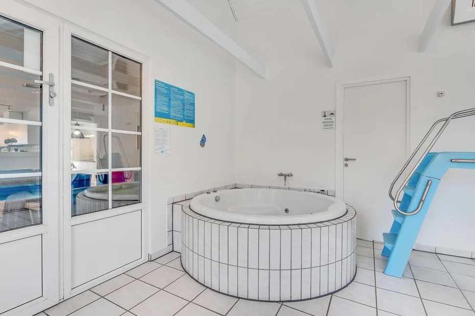 Una luminosa sala de piscina interior con una bañera redonda revestida de azulejos y escalones azules.