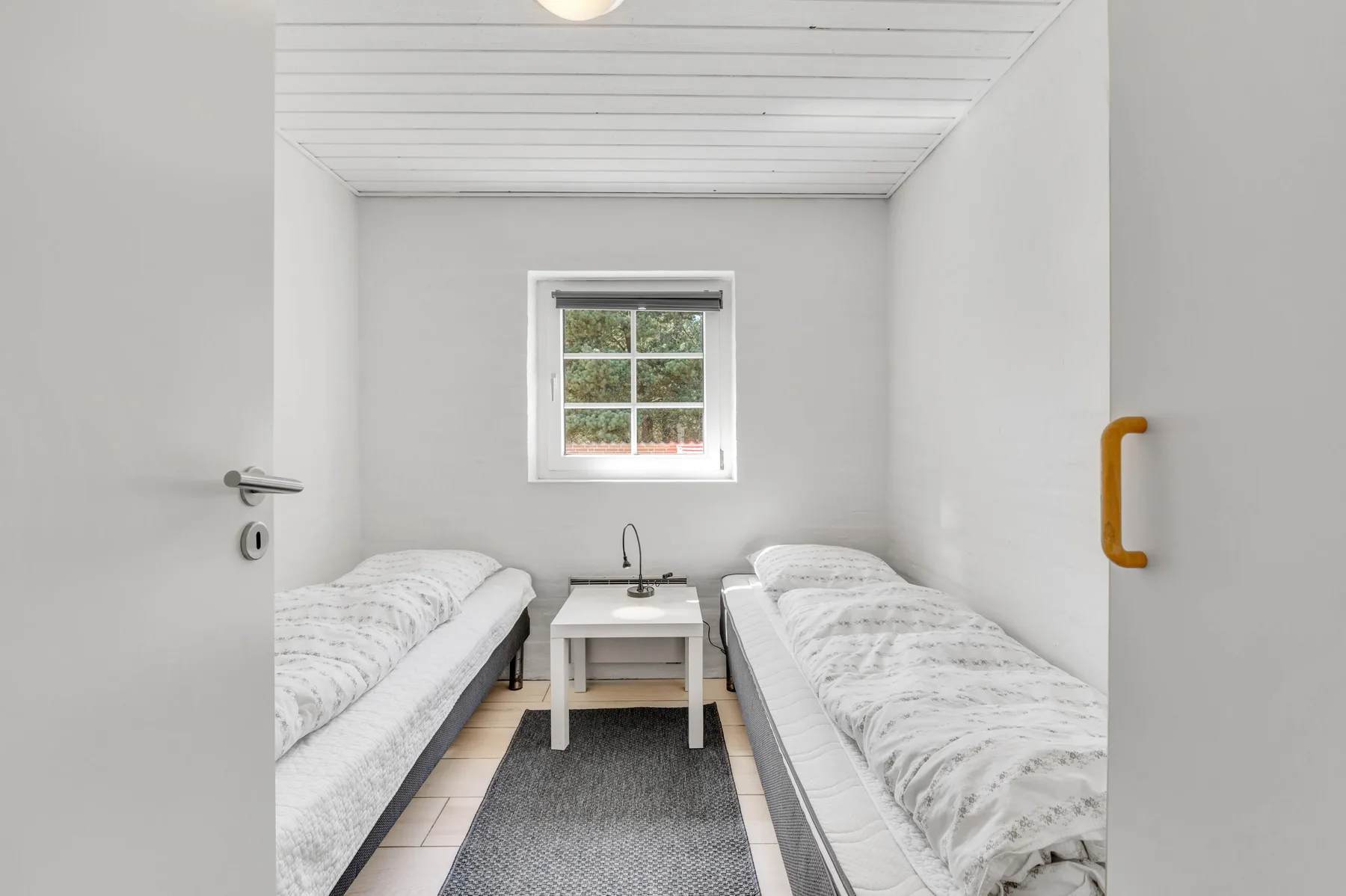 Un dormitorio con dos camas individuales, una mesita y una ventana.