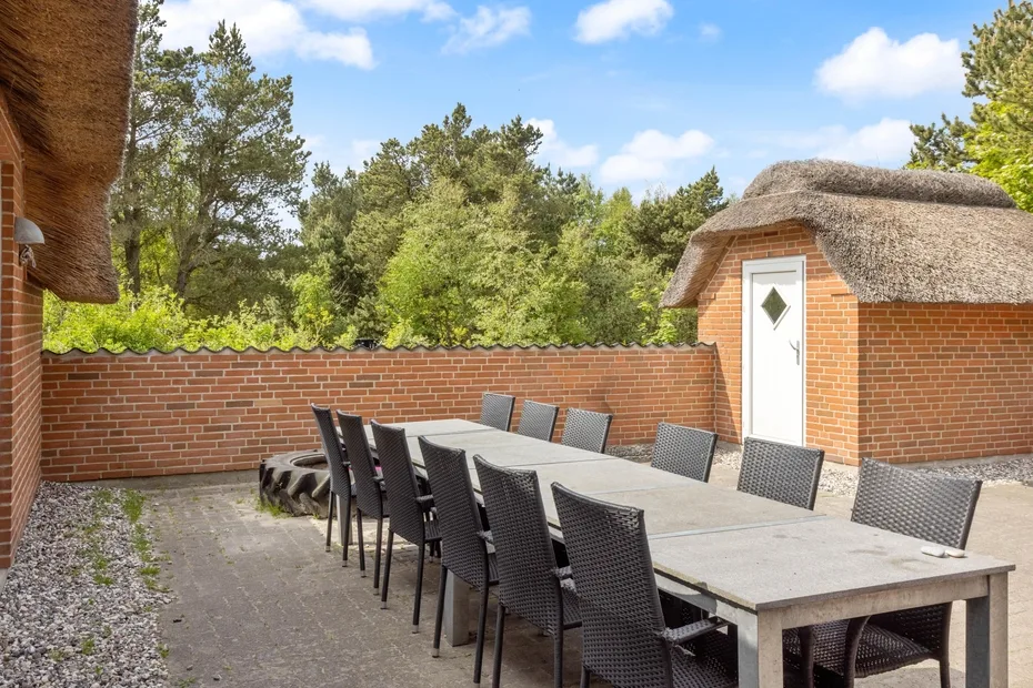 Comedor al aire libre con una mesa larga y asientos junto a un muro de ladrillo.