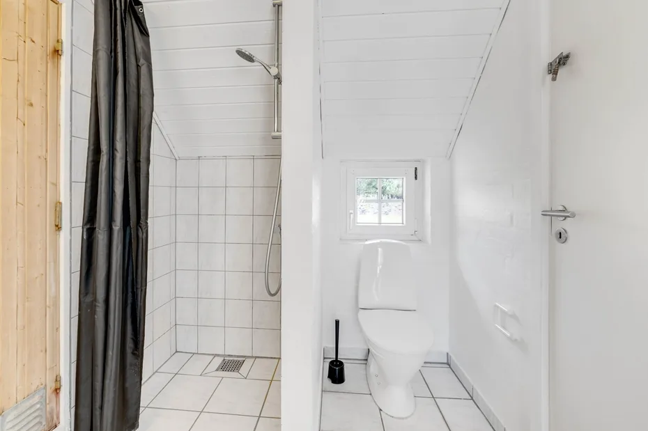 Un baño blanco con un inodoro junto a una ducha con azulejos.