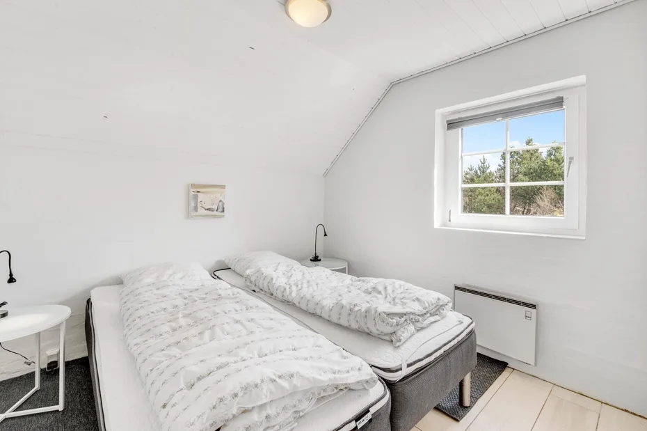 Un dormitorio con dos camas bajo un techo inclinado y una ventana.