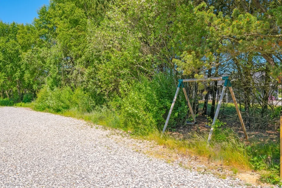 Un camino de grava bordea árboles frondosos y un columpio de madera.