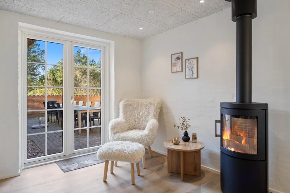 Una sala luminosa con chimenea, un sillón y puertas de vidrio que dan a un patio.