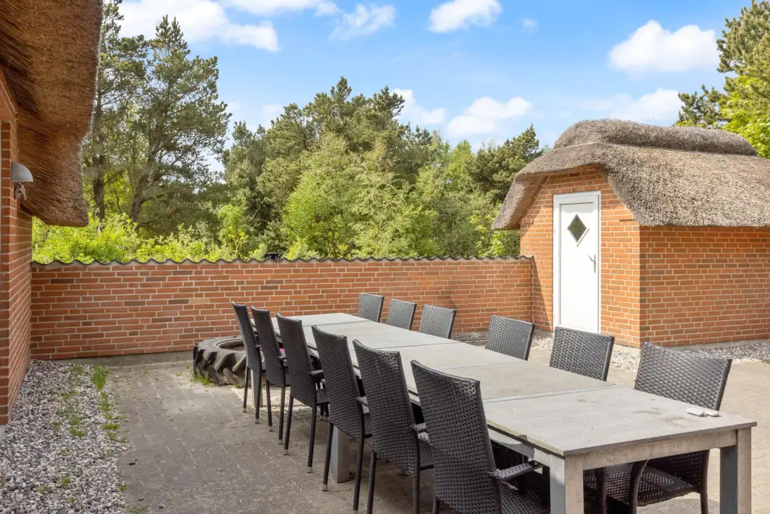 Comedor exterior con paredes de ladrillo, una mesa larga y asientos alrededor.