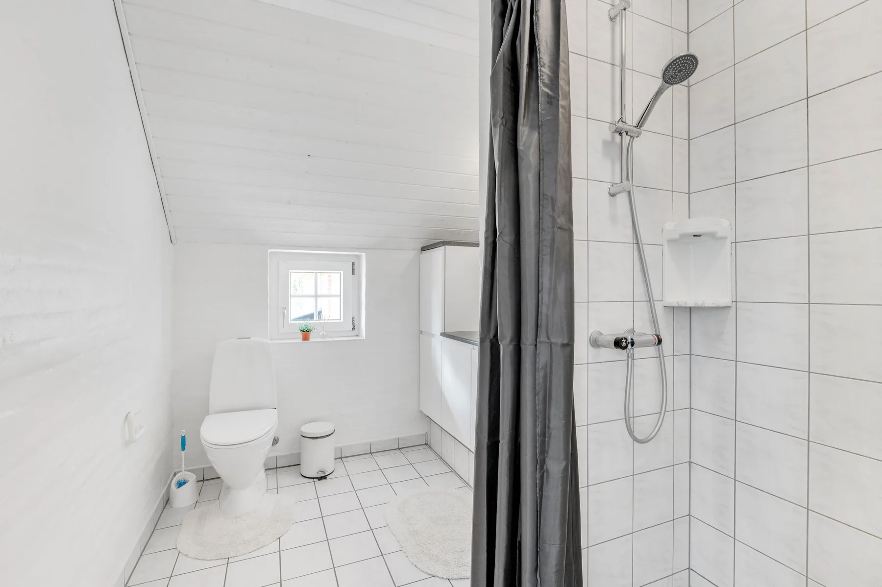 Un baño luminoso con un inodoro y una zona de ducha con azulejos.
