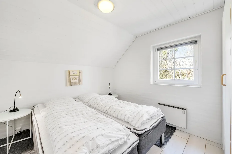 Un dormitorio luminoso con dos camas bajo un techo inclinado y una ventana.