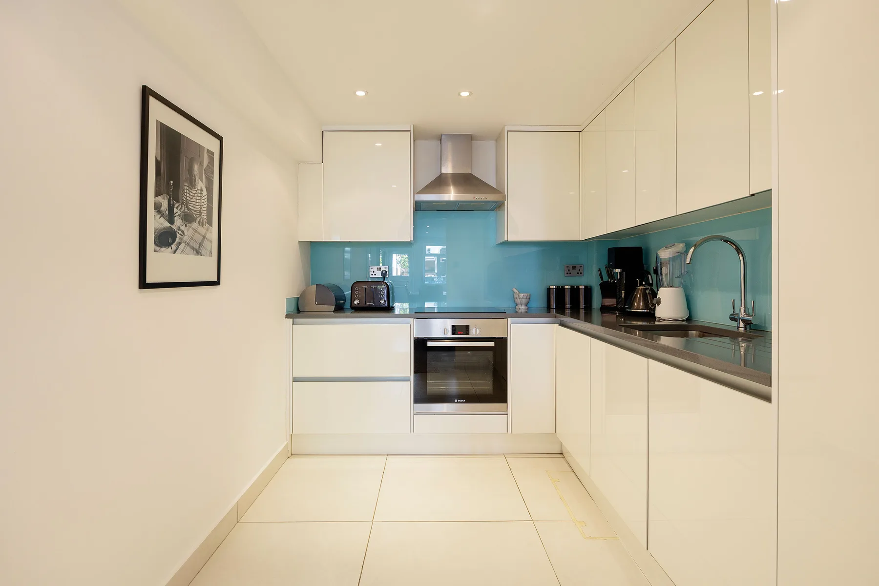 A bright modern kitchen with white cabinets and a turquoise backsplash.