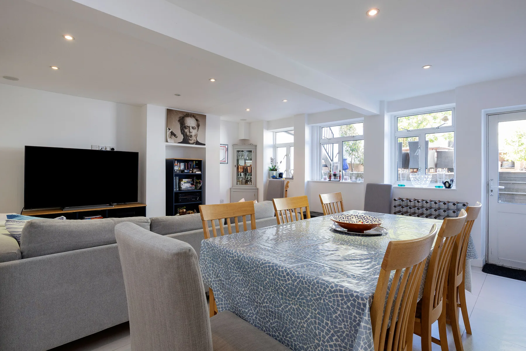 A bright dining and living area with a table, seating, and a television.