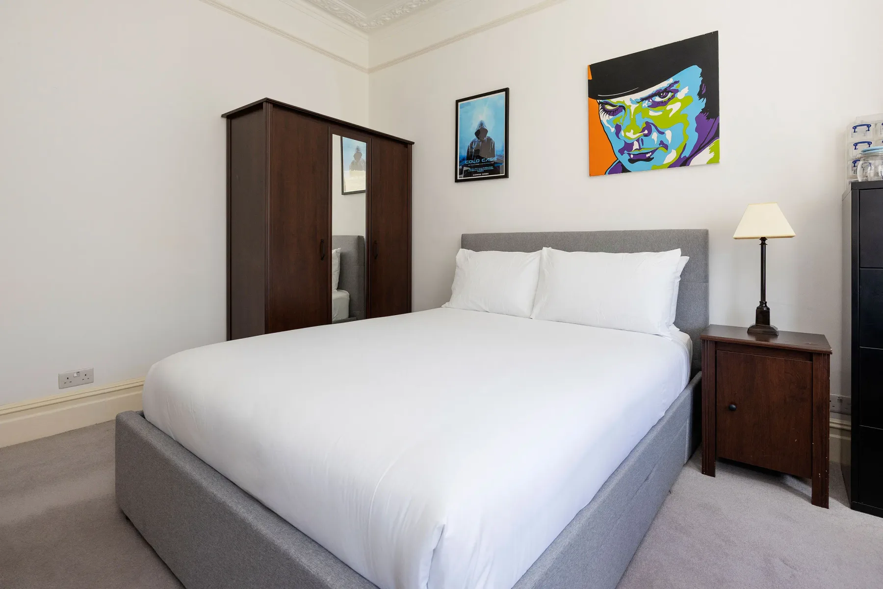 A bedroom with a large bed, bedside table, and colorful wall art.