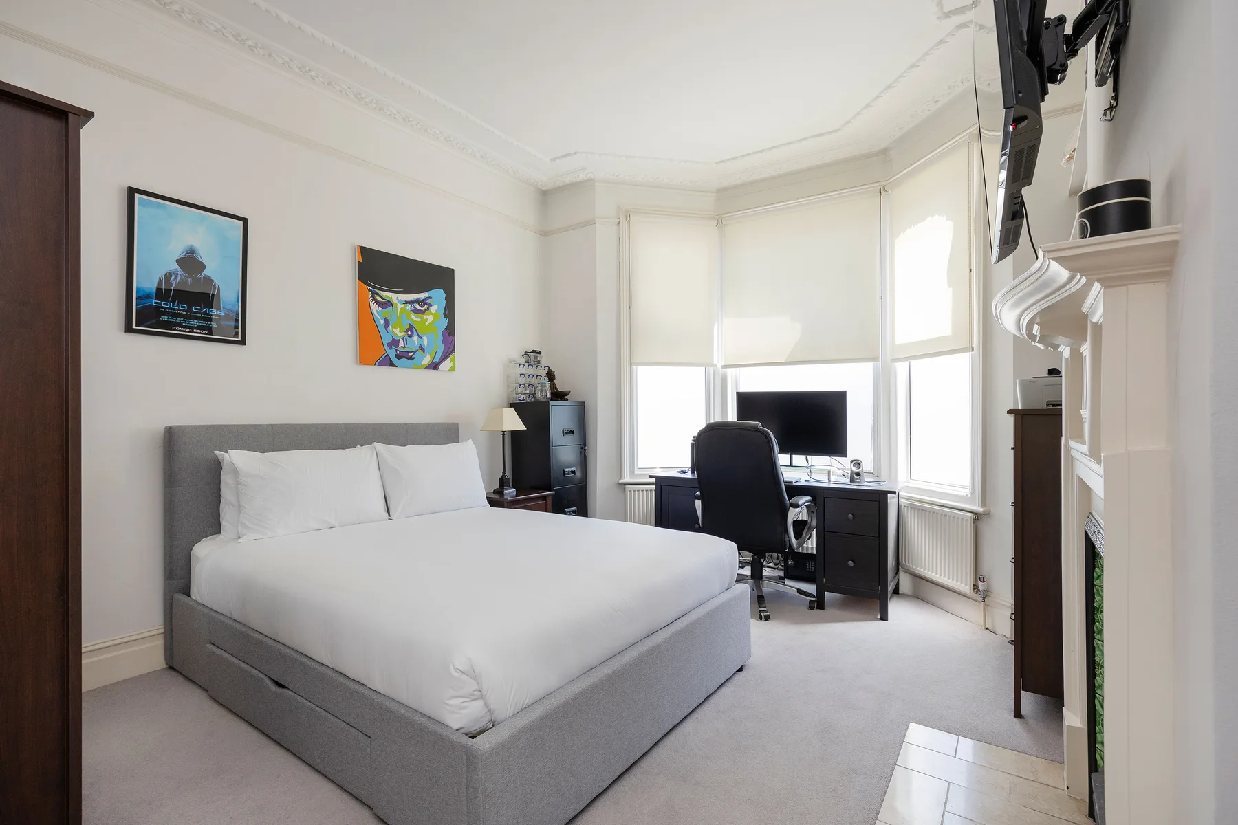 A bright bedroom with a large bed and a desk beside the windows.