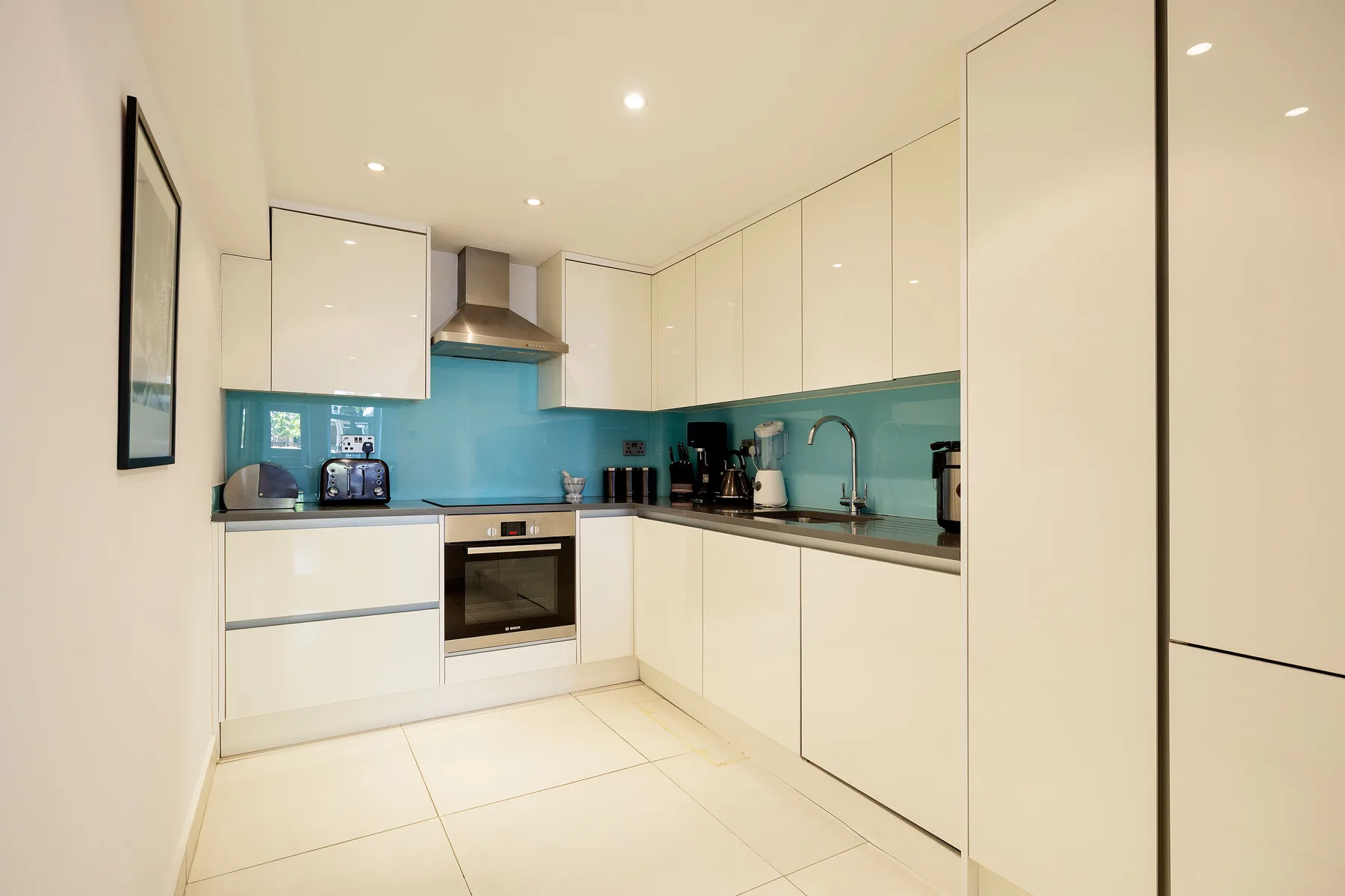 A modern kitchen with white cabinets and a turquoise backsplash.