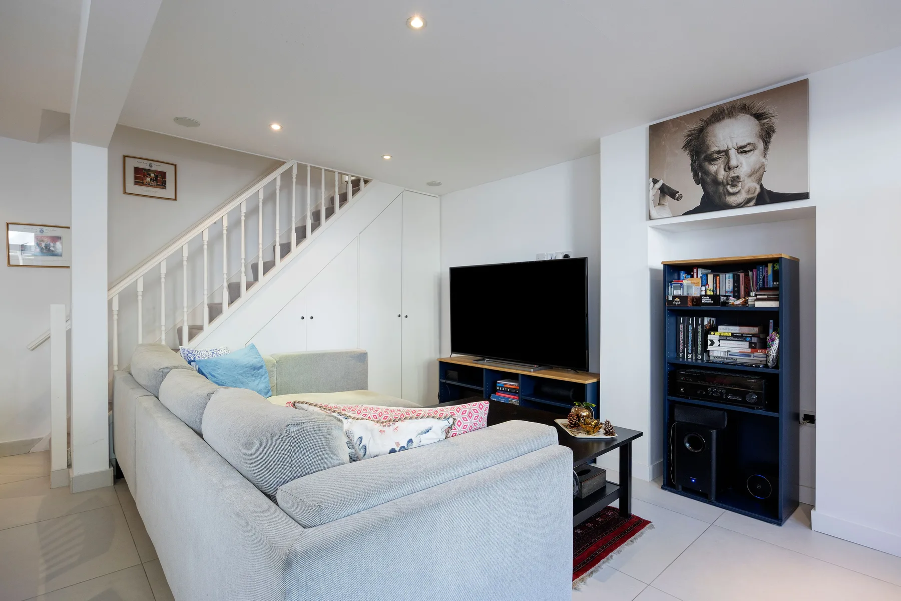 A living room with light-colored seating, a television, and a staircase.