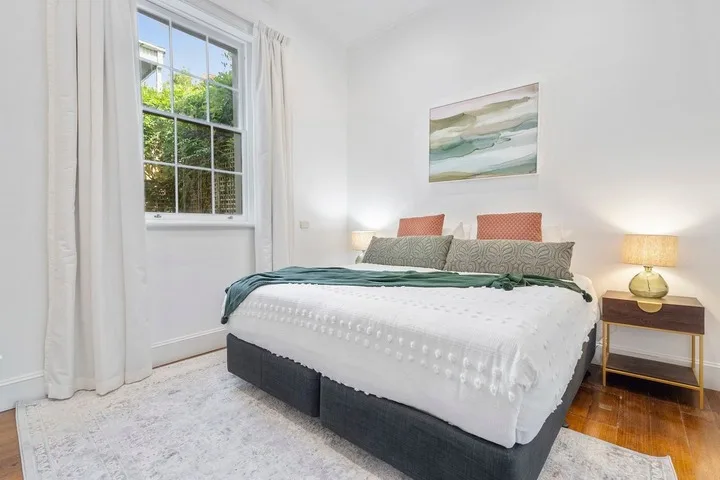 A bright bedroom with a bed, bedside tables, and a window.
