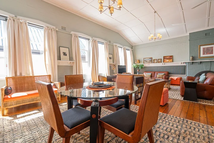 A dining area with a round table and chairs beside tall curtained windows.