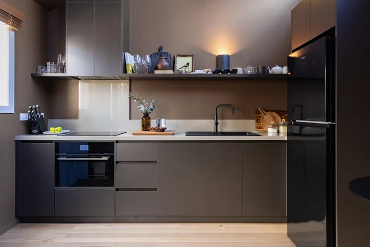 A modern kitchen with dark cabinets, a long counter, and a refrigerator.