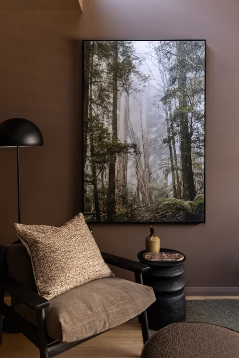 A quiet sitting area features an armchair beneath a framed forest print.