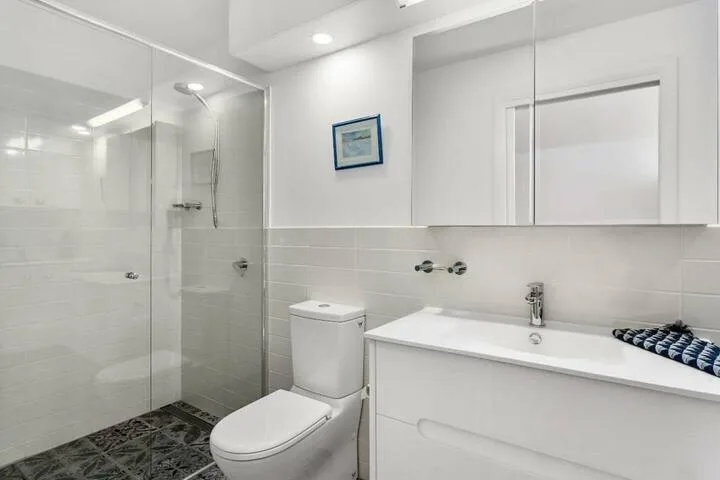 A bright bathroom with a glass shower, toilet, and white vanity.