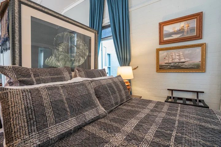 A bedroom with a patterned bedspread, blue curtains, and framed pictures.