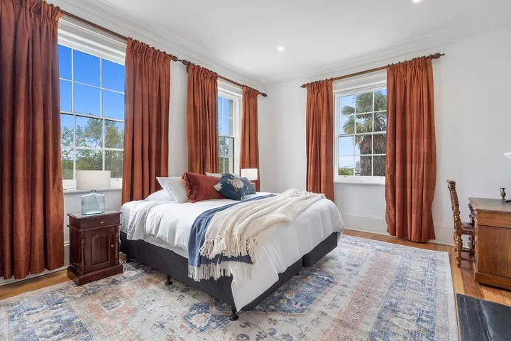 A bedroom with a bed, rust-colored curtains, and a patterned rug.
