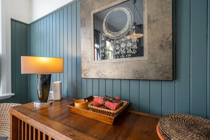 A wooden console table sits against a teal paneled wall beneath a large mirror.