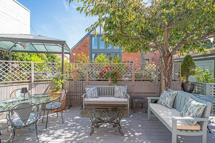 A furnished outdoor patio with a dining table, seating, and a leafy tree.