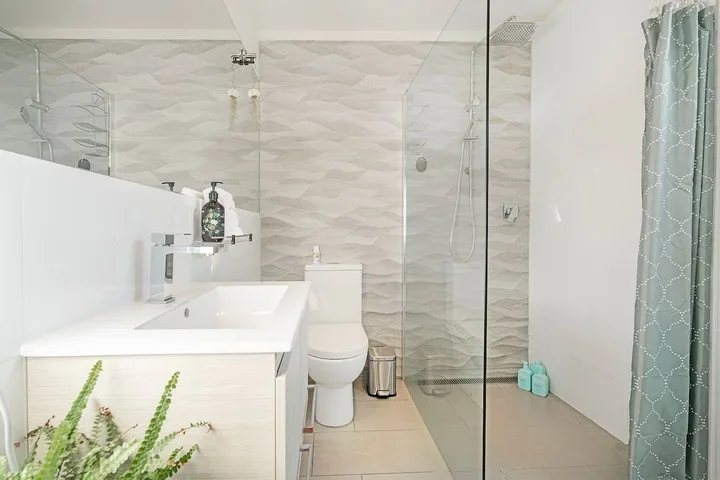 A bright bathroom with a sink, toilet, and glass shower.