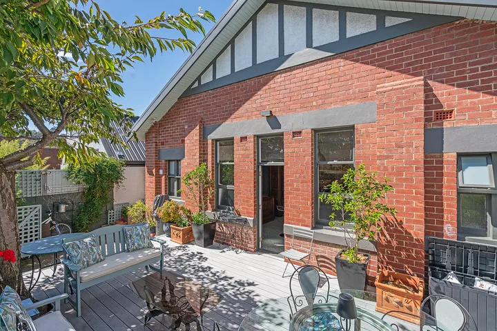 A brick building opens onto a paved patio with outdoor seating and potted plants.