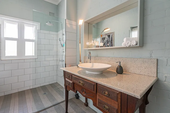 A bright bathroom with a large vanity, vessel sink, and glass shower screen.
