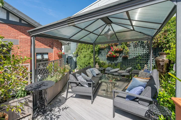 A covered outdoor seating area with gray cushions and greenery.