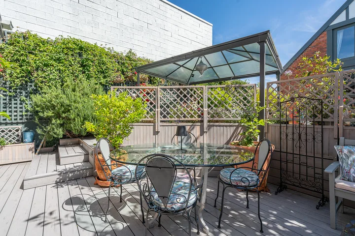 An outdoor patio with a glass-top dining table beneath a canopy.