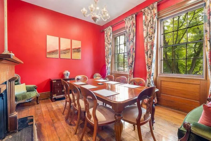 A dining room with a long wooden table, chairs, and large windows.