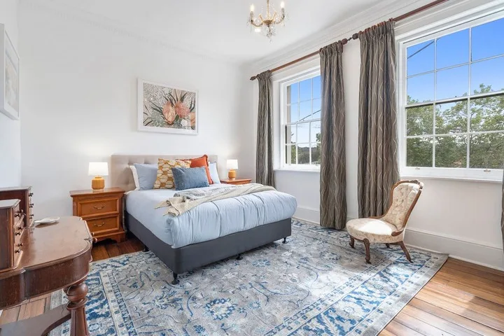 A bedroom with a bed beside tall windows and a patterned rug.