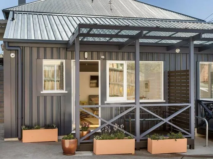 A metal-sided building has a covered porch with cross-braced railings and planters.