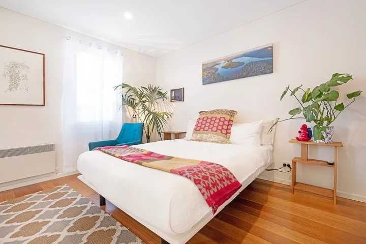 A bright bedroom with a white bed, colorful bedding, and plants.