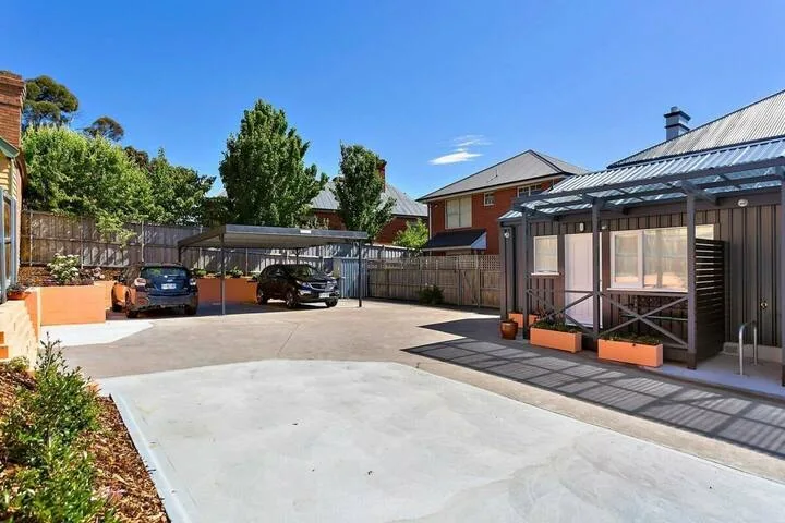 A paved outdoor courtyard with parked cars and a covered seating area.