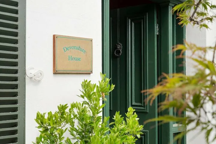 A dark green entrance door is set beside a wall-mounted name plaque and leafy plants.