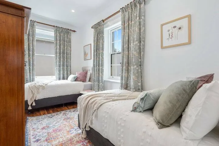A bedroom with two beds, patterned curtains, and a colorful rug.