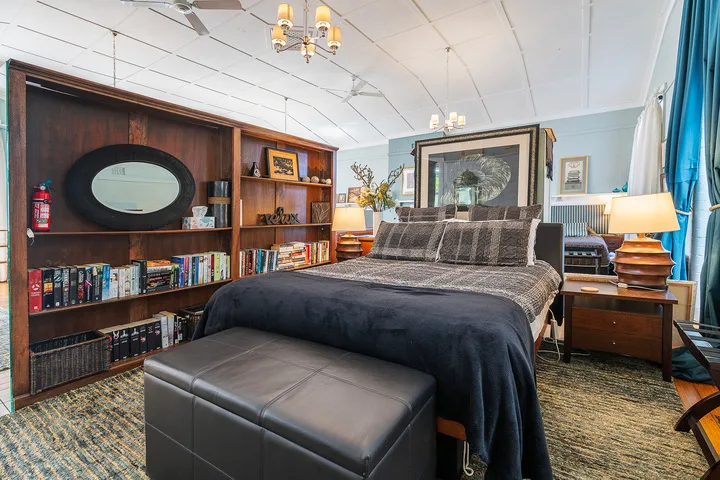 Un dormitorio con una cama oscura, un banco y estanterías empotradas.