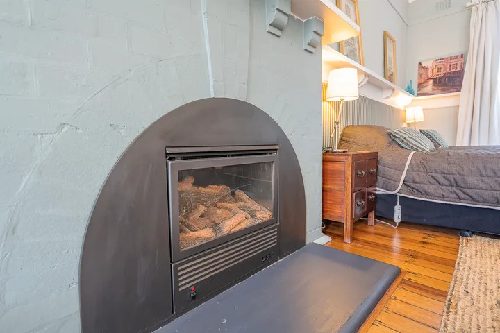 A bedroom with a bed, wooden floor, and fireplace in the foreground.