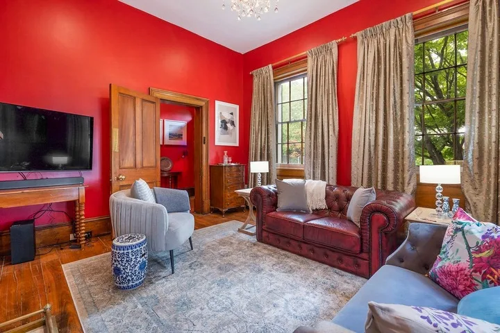 A living room with red walls, seating, and tall curtained windows.