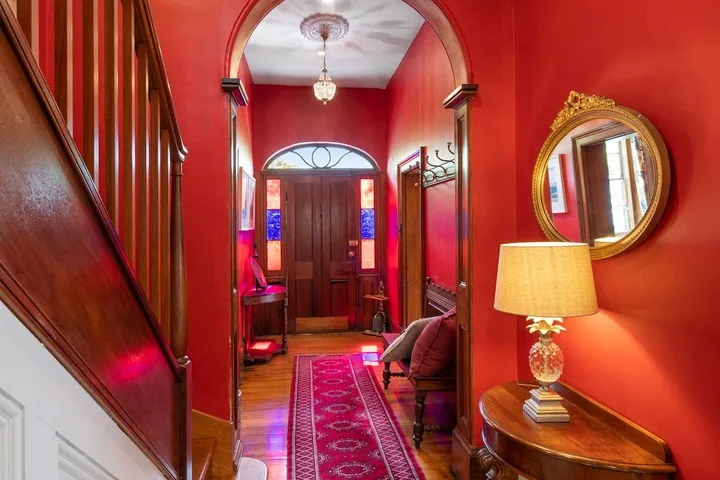 A red entry hall with a patterned runner and a wooden front door.