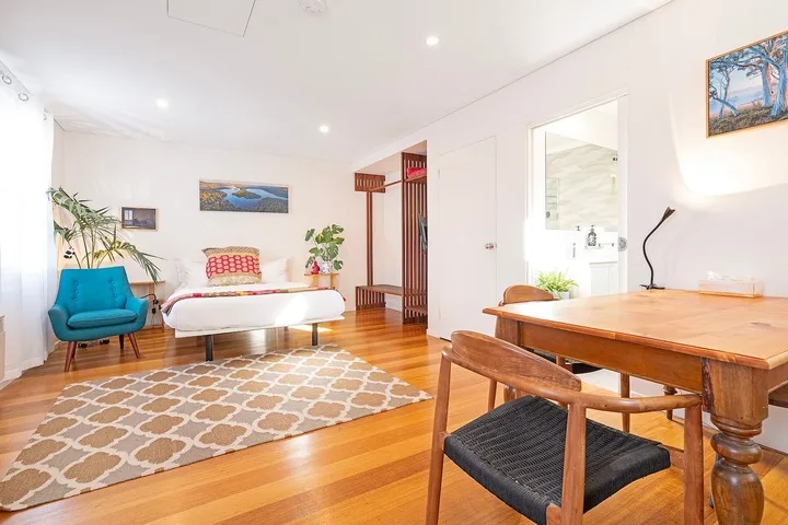 A bright bedroom and dining area with a bed, table, and wooden flooring.