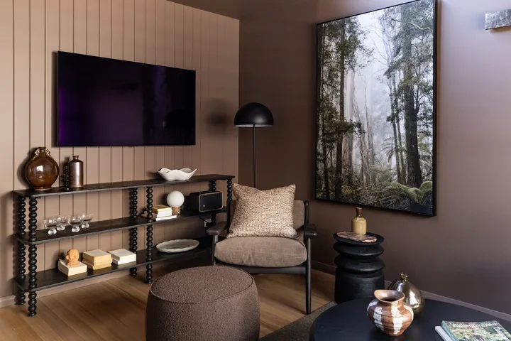A modern living room with a television, seating, and a large forest print.