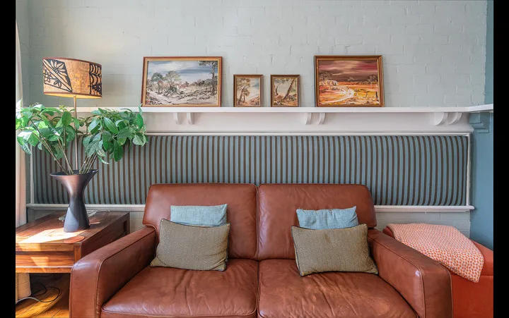 A living room with a brown leather sofa beneath a shelf of framed artwork.