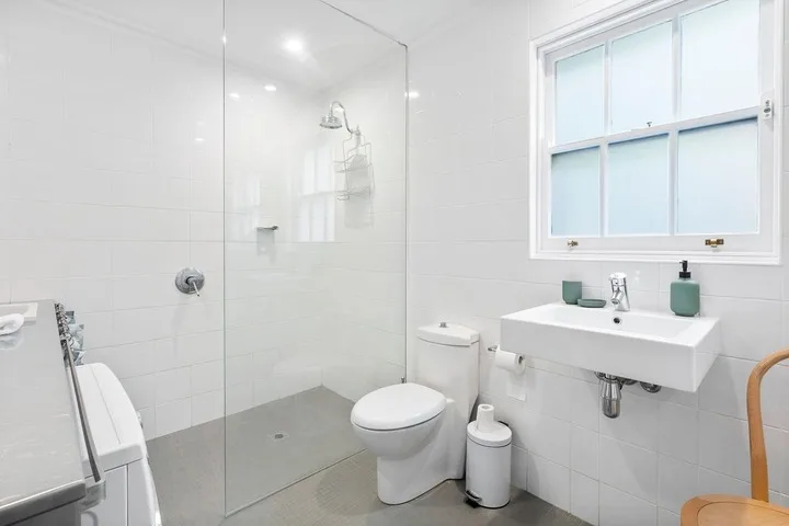 A bright tiled bathroom with a shower, toilet, and wall-mounted sink.