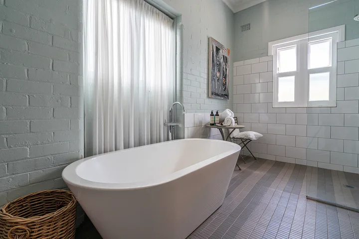 A bright bathroom features a freestanding bathtub beside a curtained window.