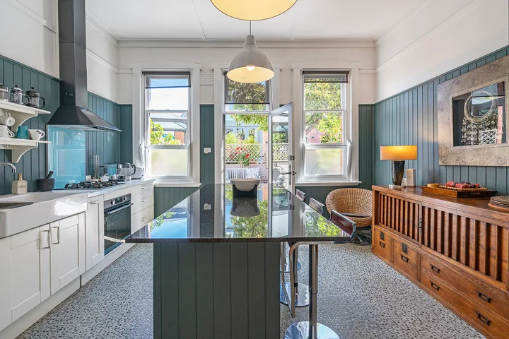 A bright kitchen with a central island and tall windows opening onto greenery.